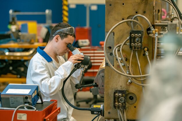 L'ingénieur vérifie le réglage correct du moule métallique pour les pièces moulées en usine à l'aide d'un microscope