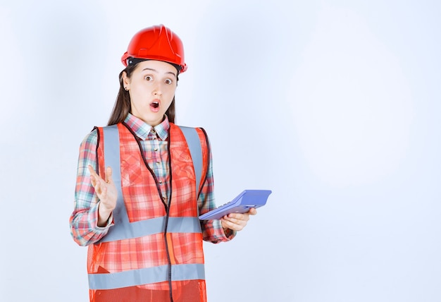 Ingénieure en casque rouge travaillant sur une calculatrice et semble confuse ou ravie.