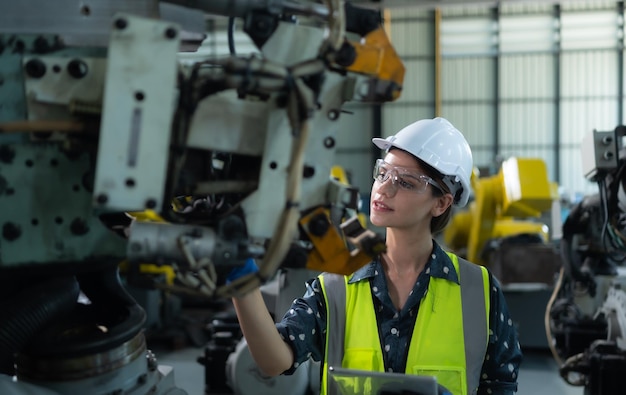 Une ingénieure installe un programme sur un bras robotique dans un entrepôt de robots et teste le fonctionnement avant d'envoyer la machine au client