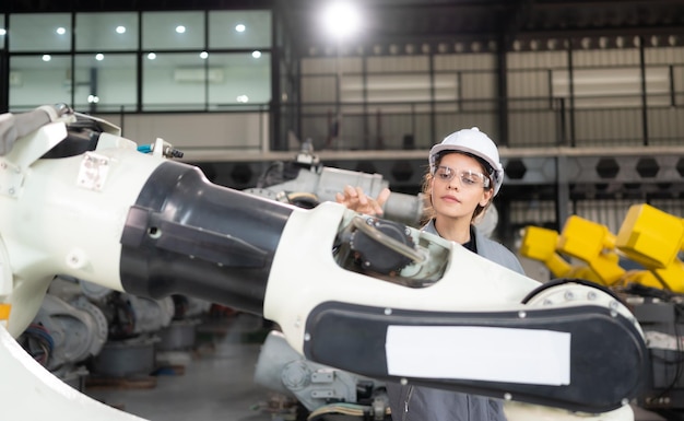 Une ingénieure installe un programme sur un bras robotique dans un entrepôt de robots et teste le fonctionnement avant d'envoyer la machine au client