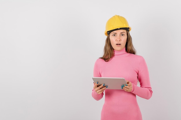 Une ingénieure surprise regarde la caméra en tenant un ordinateur planhet sur fond blanc