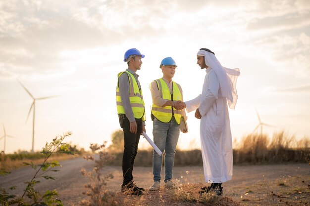 Ingénieurs asiatiques et homme d'affaires arabe vérifiant et inspectant la construction avec l'opération des gens du ciel au coucher du soleil Éolienne pour l'électricité de l'énergie propre et de l'environnement Industriel du durable