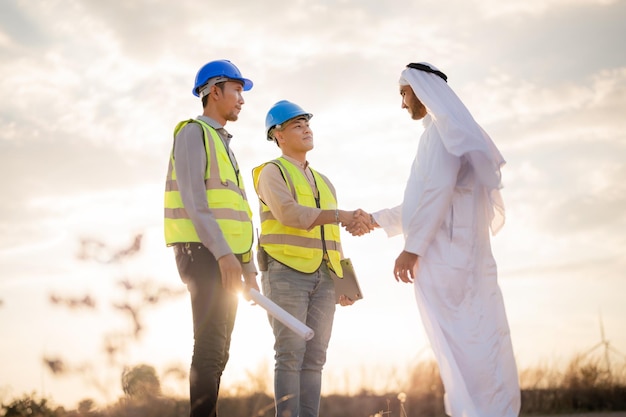 Ingénieurs asiatiques et homme d'affaires arabe vérifiant et inspectant la construction avec l'opération des gens du ciel au coucher du soleil Éolienne pour l'électricité de l'énergie propre et de l'environnement Industriel du durable