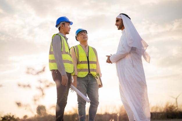 Ingénieurs asiatiques et homme d'affaires arabe vérifiant et inspectant la construction avec l'opération des gens du ciel au coucher du soleil Éolienne pour l'électricité de l'énergie propre et de l'environnement Industriel du durable