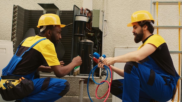 Photo des ingénieurs compétents assemblent un indicateur de pression professionnel pour vérifier les liquides et les gaz dans le climatiseur tandis qu'un mécanicien afro-américain nettoie la couche de saleté et de poussière accumulée dans le condenseur