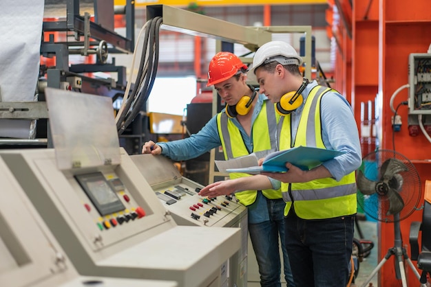 Ingénieurs masculins en gilet de sécurité avec casque discutant lors de la vérification et de la réparation de la machine en usine