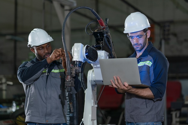 Ingénieurs masculins réparant et inspectant la machine de soudage à bras robotisé avec ordinateur portable à l'usine