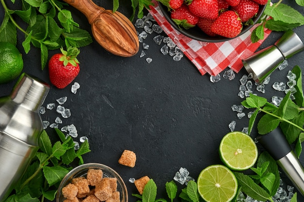 Ingrédients alimentaires frais pour faire de la limonade, de l'eau de désintoxication infusée ou un cocktail. Fraises, citron vert, menthe, basilic, sucre de canne, glaçons et shaker sur fond de pierre noire ou de béton. Vue de dessus.