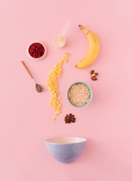 Ingrédients d'avoine, banane, avoine, framboises, graines de chia, noix, poudre de protéines et cornflakes sur fond pastel.