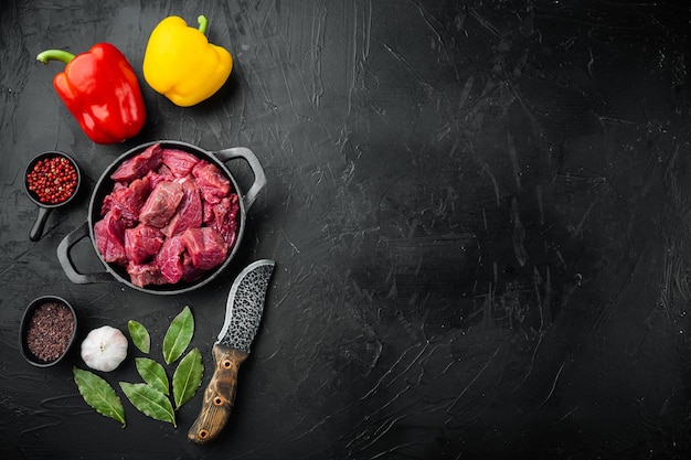 Ingrédients crus de ragoût de boeuf avec poivron doux, dans une poêle à frire en fonte, sur fond noir en pierre, vue de dessus à plat, avec espace de copie pour le texte