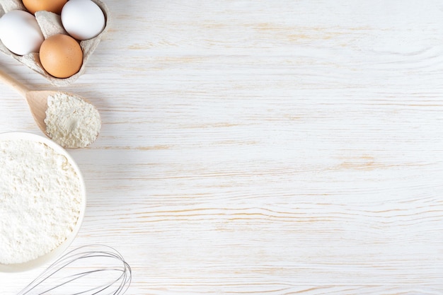 Ingrédients de cuisson farine oeufs lait ustensiles de cuisson sur fond de bois blanc avec copie espace