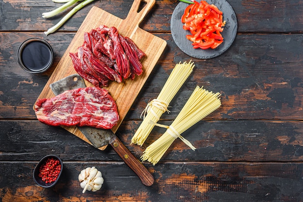 Ingrédients de cuisson pour sauté de nouilles aux légumes et au bœuf. Steak de machette et nouilles sur fond de bois. Espace pour le texte.