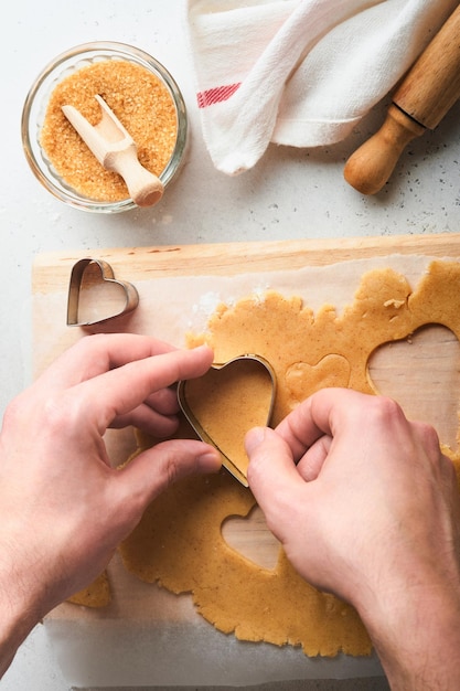 Ingrédients de cuisson et ustensiles de cuisine sur une vue de dessus de fond blanc Mains de femme ou d'homme préparant des biscuits au sucre de coeur Cuisson des biscuits au sucre Farine oeufs sucre épices sur la table de la cuisine Pose plate