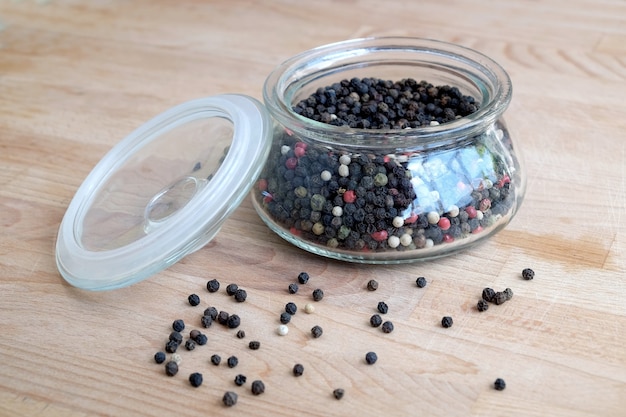 Ingrédients épicés chauds pour la nourriture. Nature morte avec des graines de poivre noir à l'intérieur d'un bocal en verre rond et éparpillés sur une table en bois