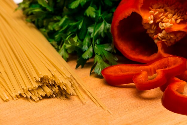 Ingrédients frais pour la cuisson : pâtes et poivrons et persil sur fond de table en bois.