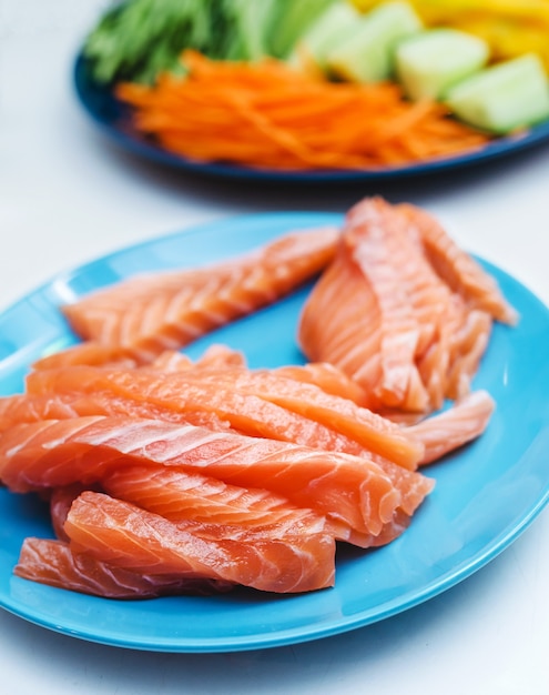 Photo ingrédients hachés comme le concombre de mangue et la carotte servis sur une assiette et prêts à préparer des sushis à côté d'un filet de saumon cru dans la cuisine d'un restaurant