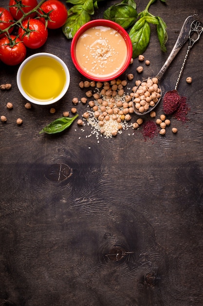 Ingrédients de l'houmous. Pois chiche, tahini, huile d'olive, graines de sésame, sumac, herbes sur fond de bois rustique foncé.