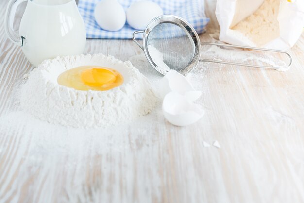 Ingrédients et outils pour la cuisson - farine, œufs et verre de lait sur la table rustique en bois. Préparation de pâtes maison