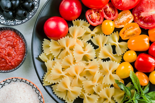 Ingrédients de pâtes, pâtes crues, tomates cerises, olives et feuilles de basilic sur la plaque noire