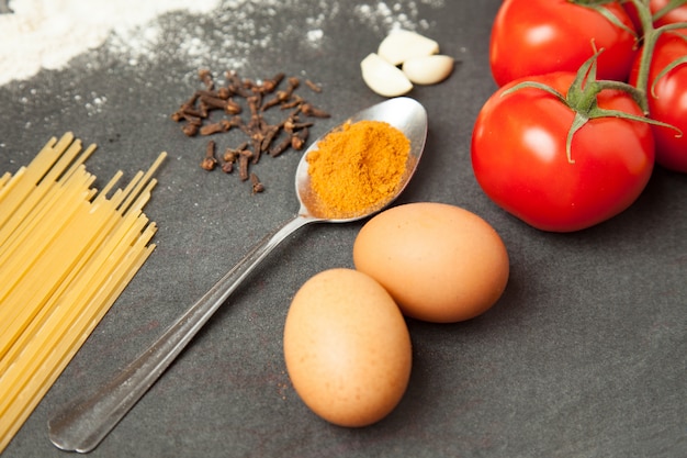 Ingrédients de pâtes. Tomates, spaghettis, ail, œufs et épices sur fond grunge noir, gros plan