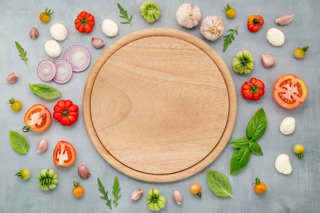 Les ingrédients de la pizza maison avec plateau à pizza en bois mis en place sur la vue de dessus de fond de béton gris