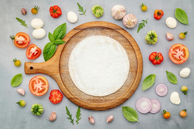 Les ingrédients de la pizza maison avec plateau à pizza en bois mis en place sur la vue de dessus de fond de béton gris