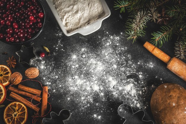 Ingrédients pour, biscuits de cuisson d'hiver. Pain d'épices, gâteau aux fruits. Farine, canneberges, oranges séchées, cannelle, épices sur une table en pierre noire, vue du dessus