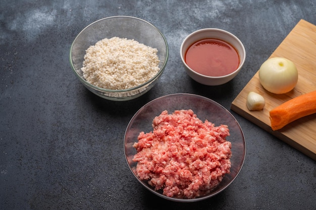 Ingrédients pour boulettes de viande viande hachée riz pâte de tomate oignon ail carottes sur une planche à découper sur un