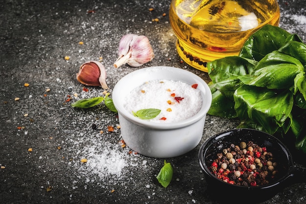 Ingrédients pour cuisiner le dîner, épices, table en pierre sombre. Feuilles de basilic, huile d'olive, ail, sel et poivre, fond