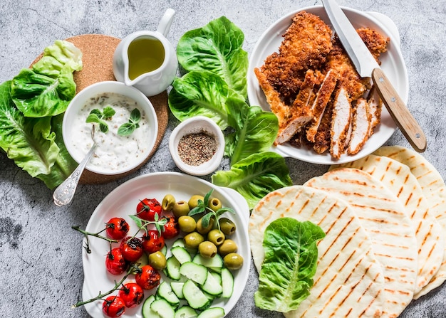 Ingrédients pour la cuisson des gyros grecs poulet schnitzel tortillas de laitue sauce au yogourt grec tomates olives sur fond gris vue de dessus