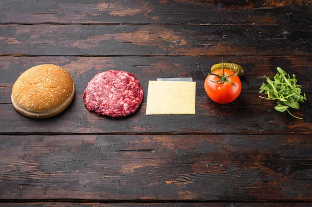 Ingrédients pour la cuisson des hamburgers. Galettes de boeuf haché, petits pains, tomates, herbes et épices, sur fond de table en bois foncé ancien, avec espace de copie pour le texte