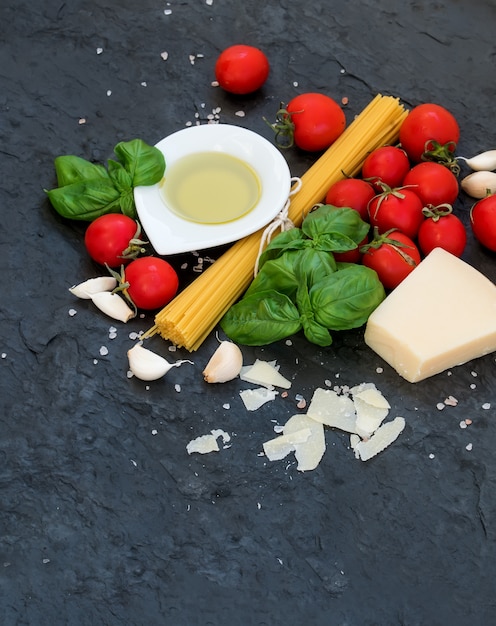 Ingrédients pour la cuisson des pâtes. Spaghetti, huile d'olive, ail, parmesan, tomates et basilic frais sur ardoise noire, vue de dessus, fond.