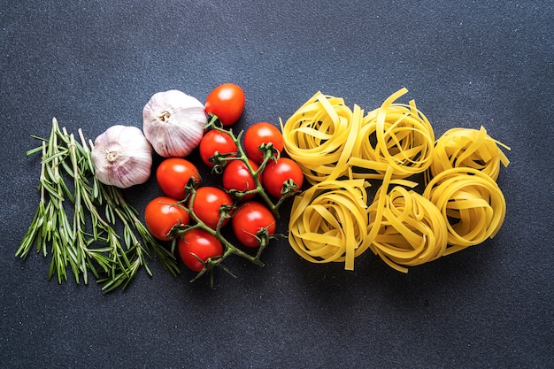 Ingrédients pour la cuisson des pâtes sur une surface sombre, vue de dessus, mise à plat. Pâtes, tomate, ail, romarin, poivre.