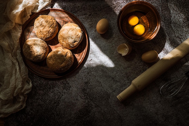 Ingrédients pour la cuisson des petits pains de seigle oeufs au rouleau à pâtisserie sur une table grise éclairée par le soleil 1