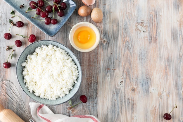 Ingrédients pour faire des boulettes de fromage cottage avec des cerises Farine d'oeufs de fromage cottage et cerises fraîches sur une table en bois Espace de copie