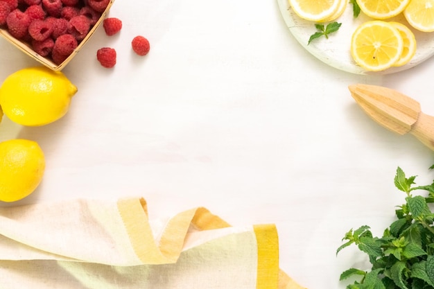 Ingrédients pour faire de la limonade aux framboises sur une table blanche.