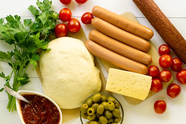 Ingrédients pour faire de la pizza à la saucisse sur un fond en bois blanc