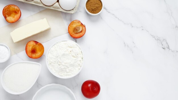 Ingrédients pour faire une tarte classique avec des prunes sur fond blanc