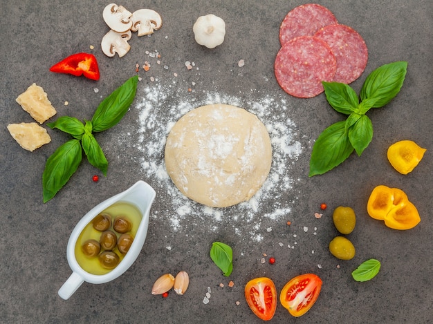 Les ingrédients pour une pizza maison avec des ingrédients sur fond de pierre sombre avec pose à plat.