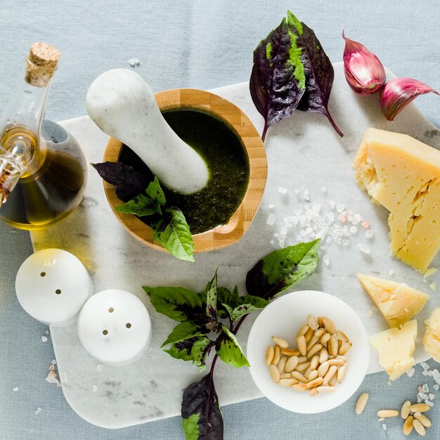 Ingrédients pour la préparation du pesto violet au basilic italien avec du fromage sur une nappe bleue en lin