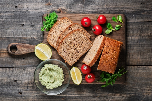 Ingrédients pour des sandwichs sains. Pain de grains entiers maison tranché, tomates cerises, salade de maïs, roquette et guacamole à l'avocat.