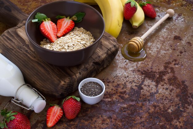 Ingrédients sains pour le petit-déjeuner : flocons d'avoine, miel, fruits, fraises et graines de chia. concept d'aliments biologiques naturels avec espace de copie.