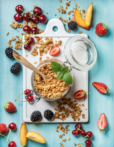 Ingrédients Sains Pour Le Petit-déjeuner Granola D'avoine Dans Un Bocal En Verre Ouvert Baies De Fruits Et Menthe Sur Fond Bleu Avec Panneau En Céramique Blanche Au Centre