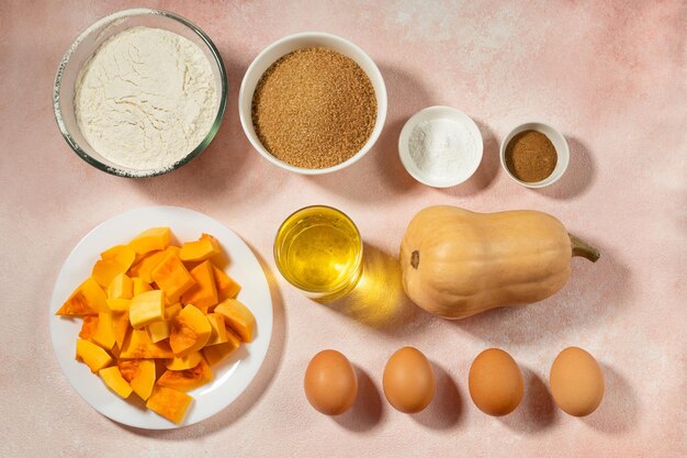 Ingrédients de la tarte à la citrouille dans des bols sur une table rose