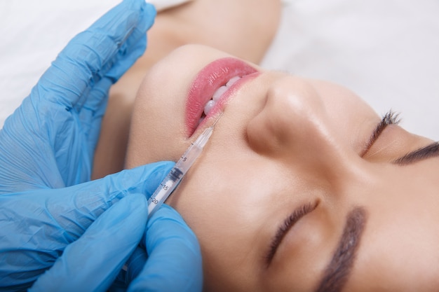 Injections de beauté pour le visage. Portrait belle jeune femme recevant une injection d'acide hyaluronique. Gros plan des mains dans les gants tenant la seringue près du visage féminin attrayant.