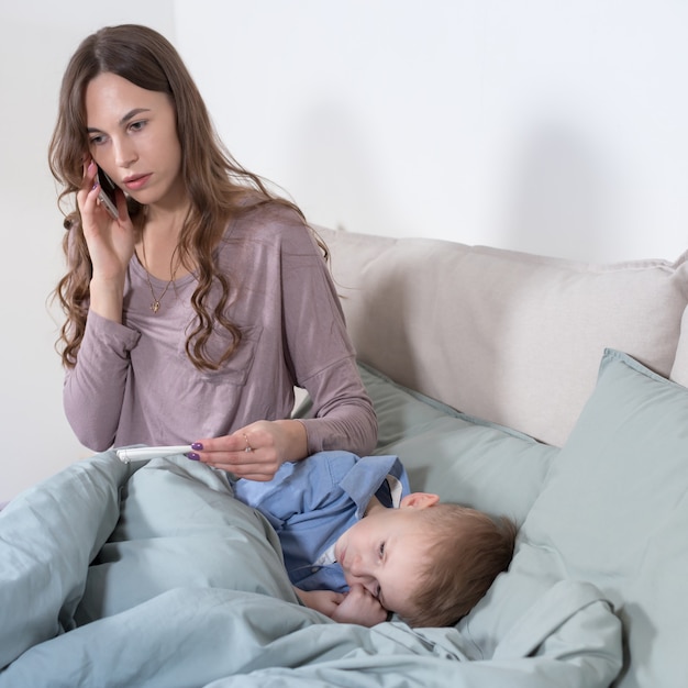 Inquiète jeune mère mesurant la température de son fils et appelant un médecin.