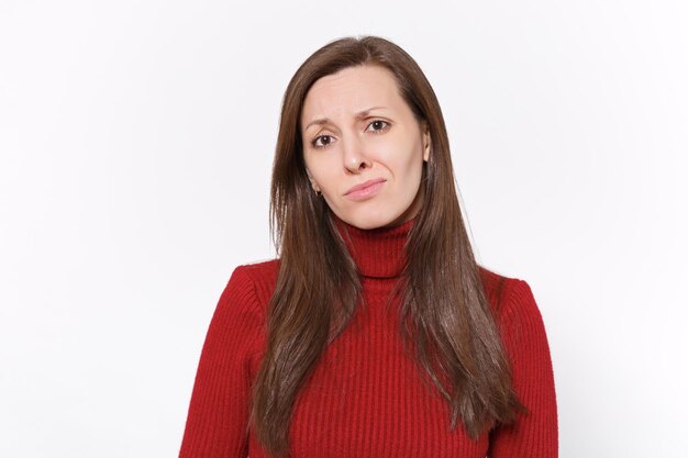 Insatisfait bouleversé jeune femme brune en vêtements rouges décontractés posant isolé sur fond blanc portrait en studio. Concept de mode de vie des émotions sincères des gens. Maquette de l'espace de copie. Regarder la caméra.