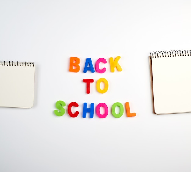 Inscription à l'école de lettres en plastique multicolores et d'une pile de cahiers avec des feuilles blanches vierges