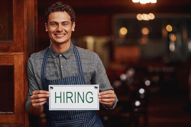 Inscription d'embauche et portrait d'un homme dans un restaurant avec un sourire opportunité et emploi au pub avec le propriétaire d'une petite entreprise café hospitalité et entrepreneur heureux à l'entrée de la brasserie avec affiche de recrutement