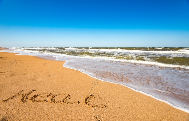 Photo l'inscription sur l'été de sable près de la vague de mer orageuse par une chaude journée d'été ensoleillée. concept des vacances d'été et des vacances tant attendues